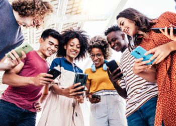Diverse teenage students using digital smart phones mobile at college campus - Group of friends watching cellphones sharing content on social media platform - Youth, friendship and technology concept